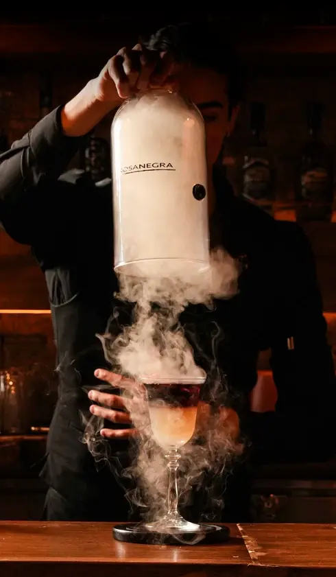 Bartender infusing a cocktail with smoke from a specialized device at a bar.