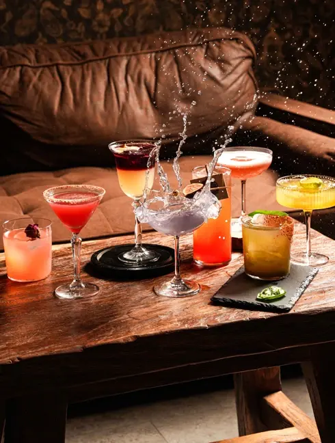 Assortment of vibrant cocktails on a dark wooden table with a sofa in Rosa Negra Miami